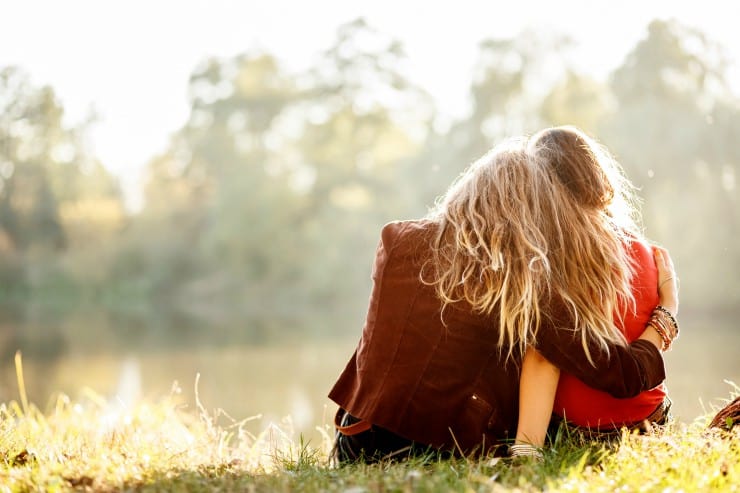two girls sitting in field hugging