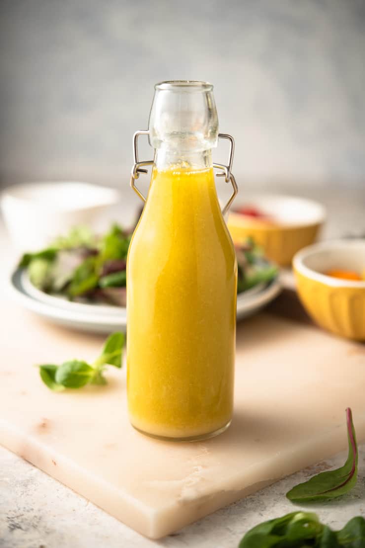 Greek dressing in a glass bottle with salad in the background