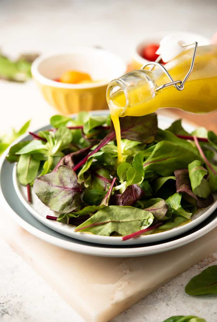 Greek dressing getting poured over a salad