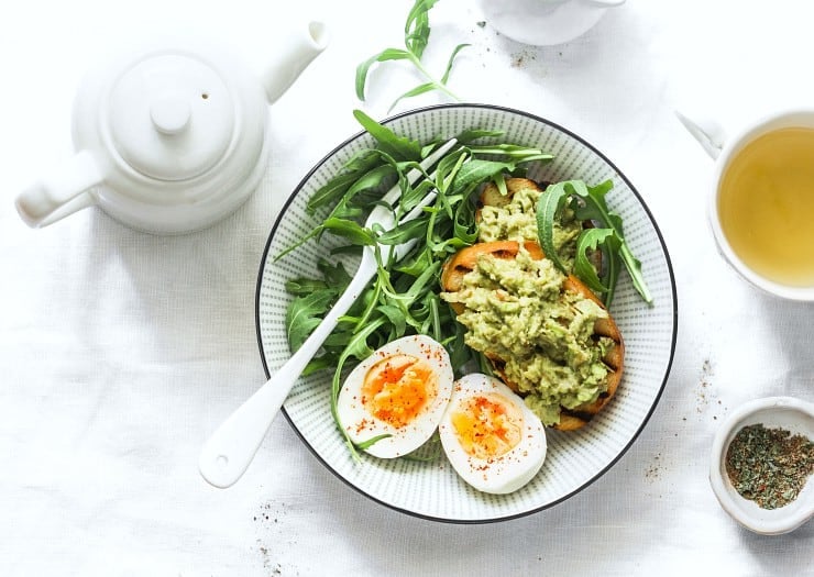 Healthy breakfast or snack - boiled egg, arugula salad and avocado toast on a light background, top view