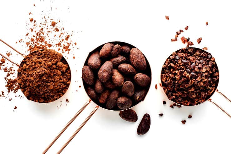 Rose gold measuring cups of cocoa beans, cacao nips and cocoa powder on a white background, flat lay healthy food concept