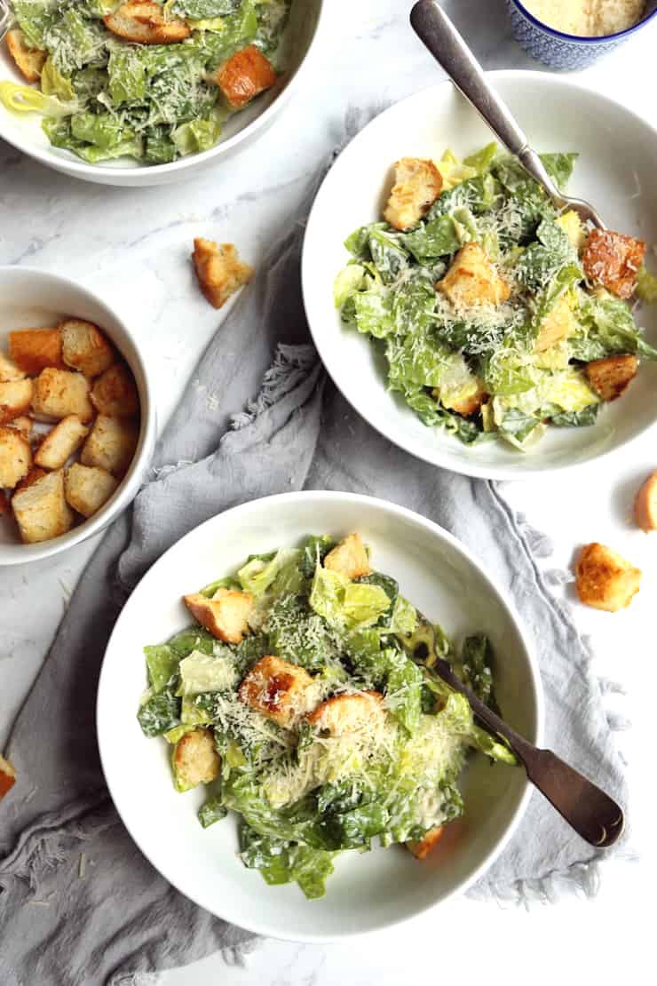 overhead view of Classic Caesar Salad with garlicky sourdough croutons in white bowls on marble background