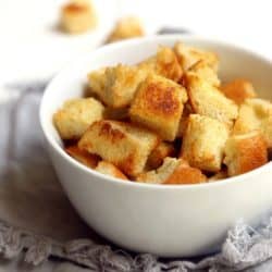 front view of white bowl full of homemade garlic butter croutons on gray napkin with white background