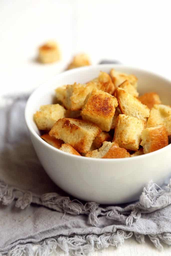 front view of white bowl full of homemade garlic butter croutons on gray napkin with white background