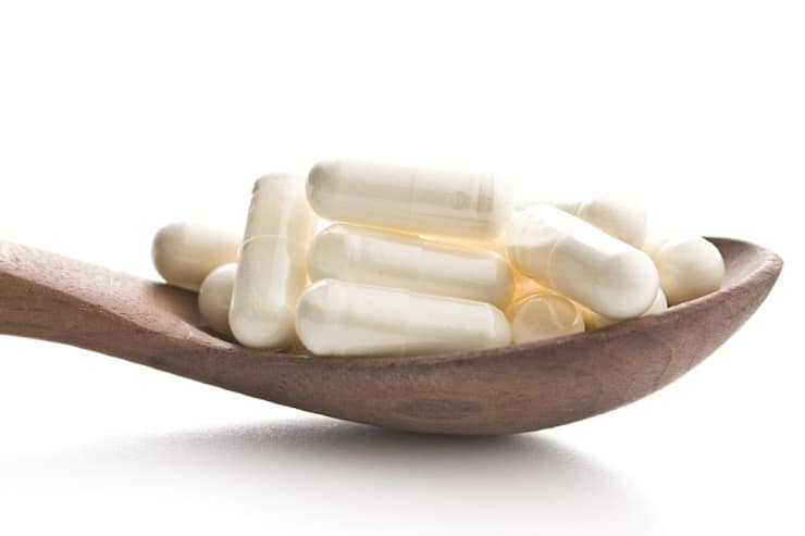 close up image of wooden spoon full of white colostrum capsules