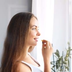 Happy young woman looking out apartment window, taking dietary supplements