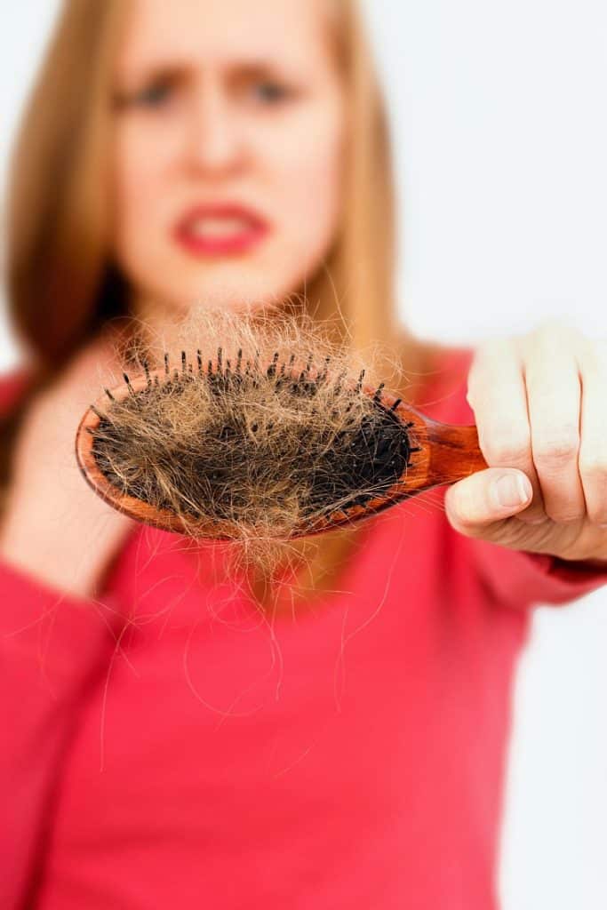 Woman holding hair brush full of hair that fell out