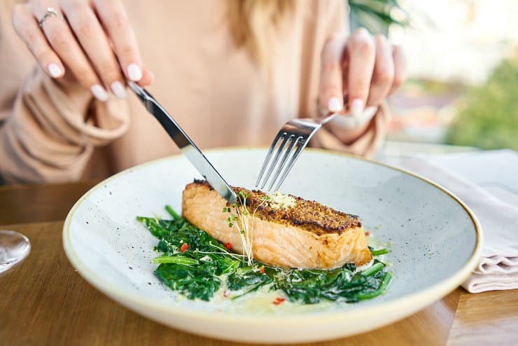 close up of woman cutting into salmon steak on a bed of spinach