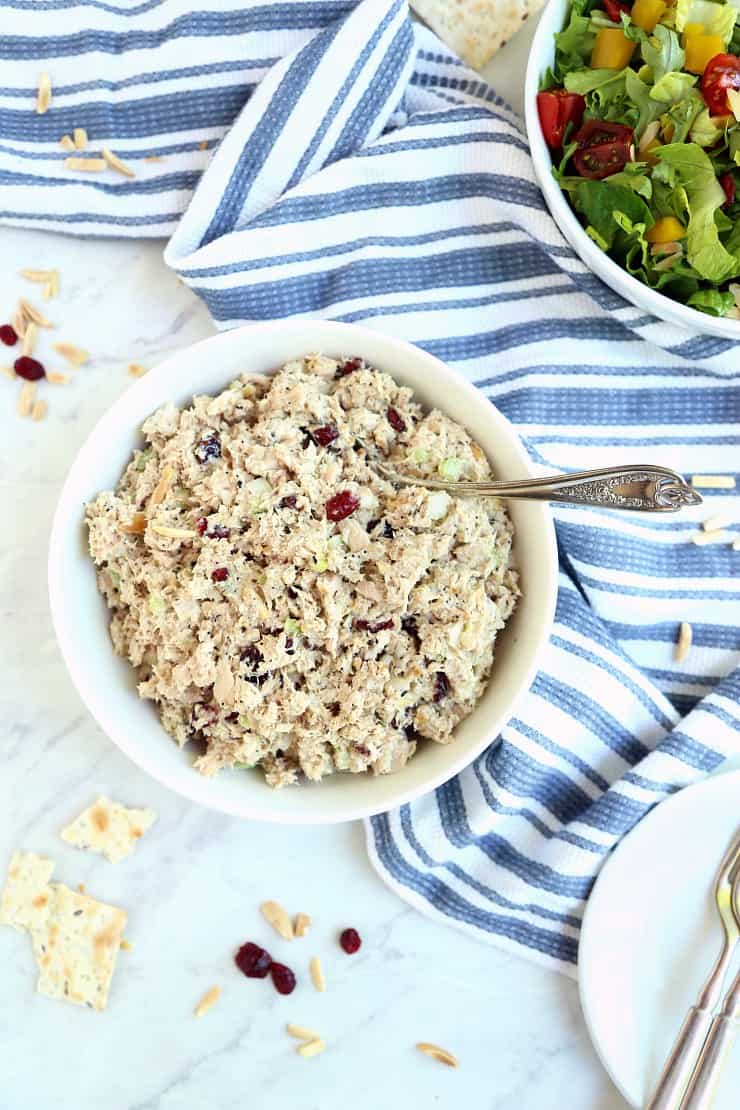 Overhead image of tuna salad in white bowl with blue and white napkin and bowl of salad greens in background