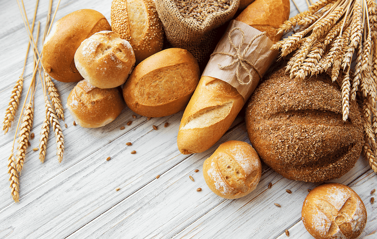 overhead image of various gluten containing breads on a white wood background