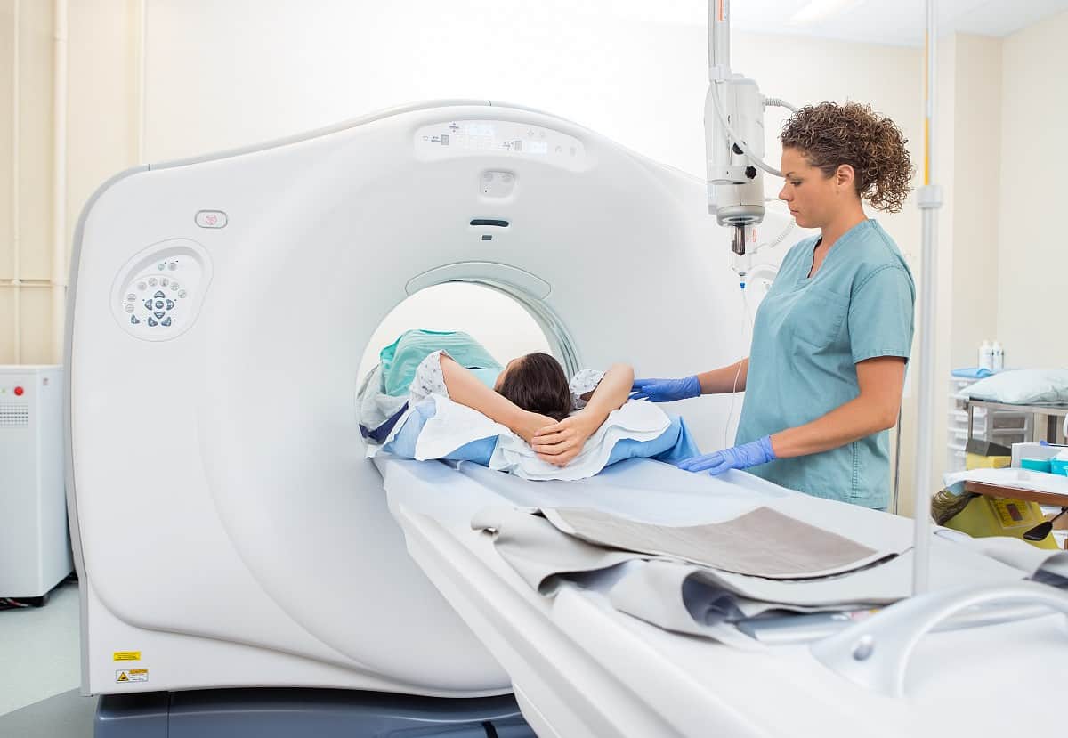 medical technician helping woman enter CT machine for abdominal scan