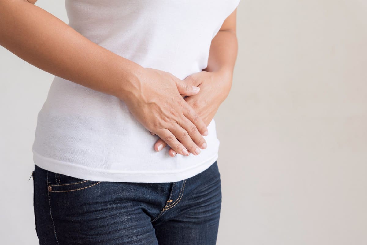 close up image of woman holding her stomach in pain