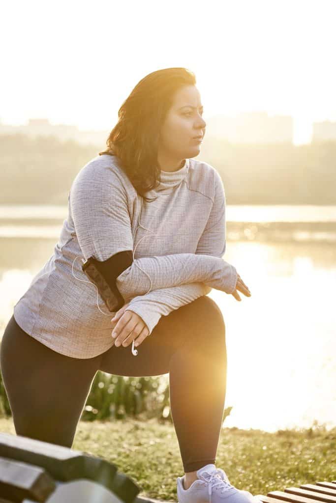 Brunette woman stretching on bench in middle of her morning run