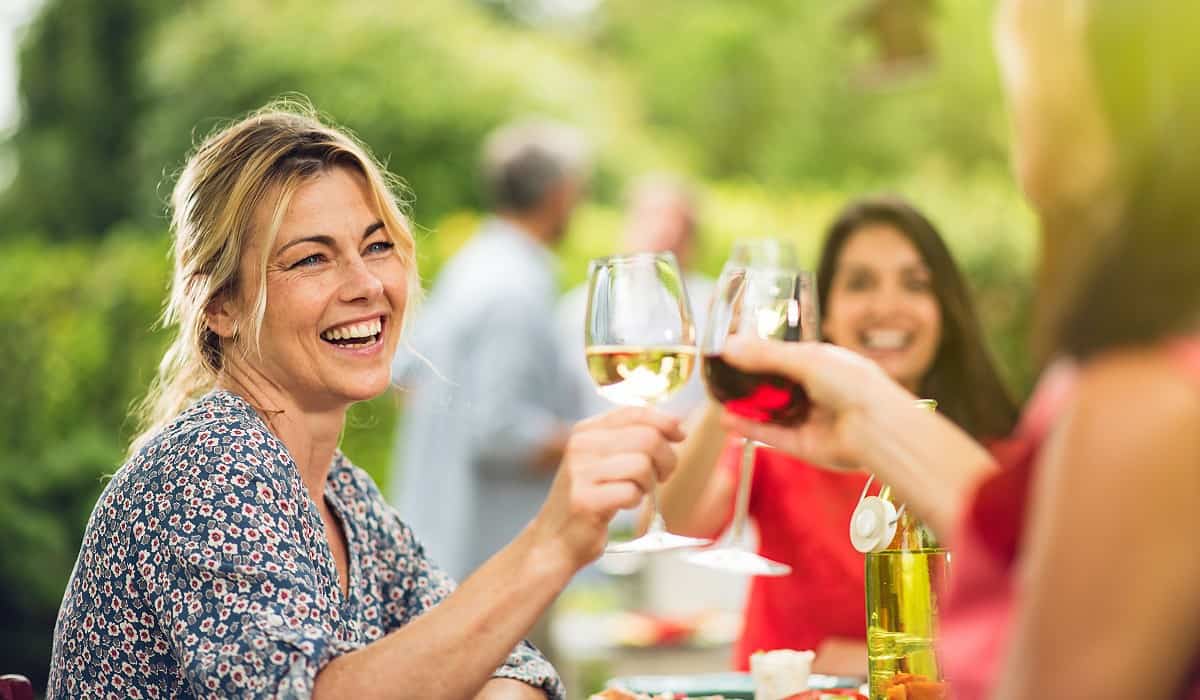 group of women at outdoor dinner laughing and raising toast with glasses of wine