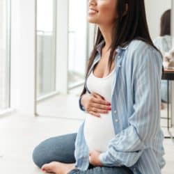 Pregnant woman smiling and holding her belly on floor of sunlit apartment