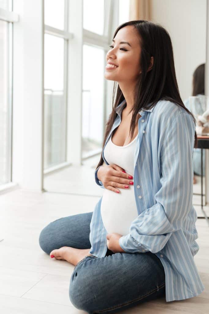 Pregnant woman smiling and holding her belly on floor of sunlit apartment