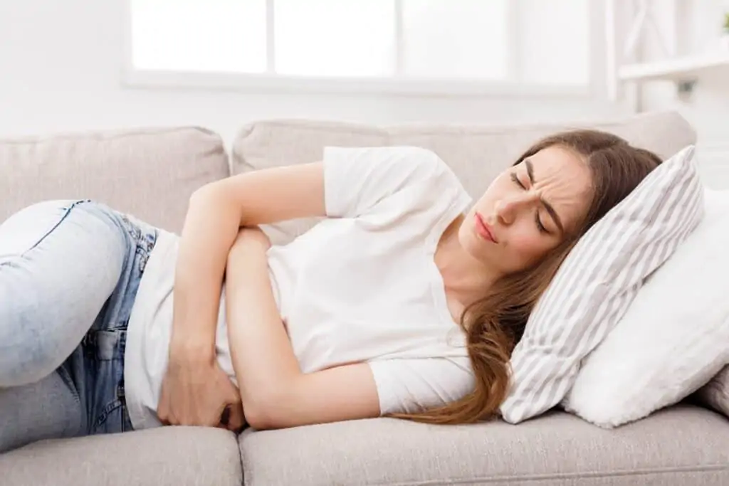 young brunette woman lying down on couch, holding her stomach in pain