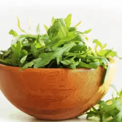 close up image of wooden bowl of arugula leaves on white background