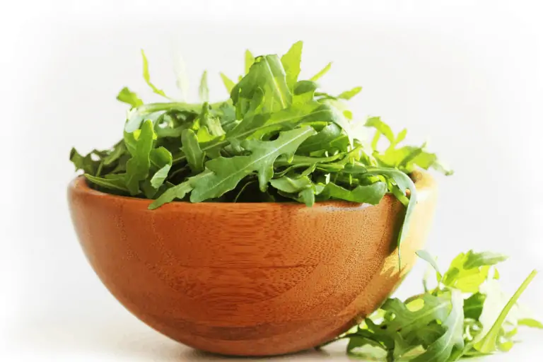 close up image of wooden bowl of arugula leaves on white background