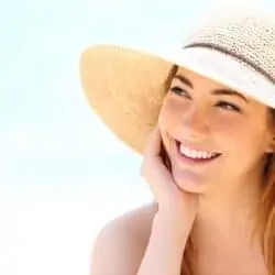 Beautiful brunette woman with sun hat smiling on the beach