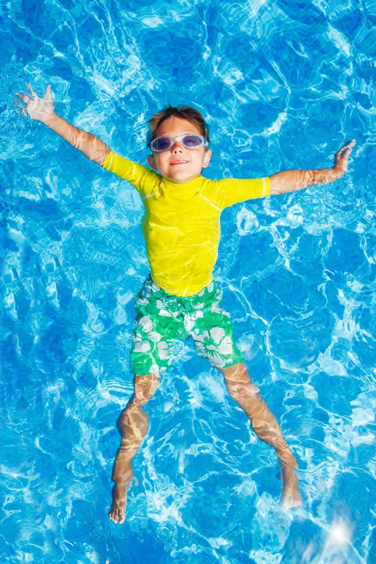 Overhead view of young boy swimming in pool wearing sun protective rash guard 