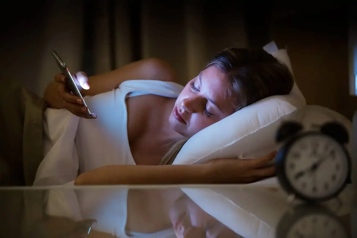 Woman lying in bed with insomnia scrolling her phone