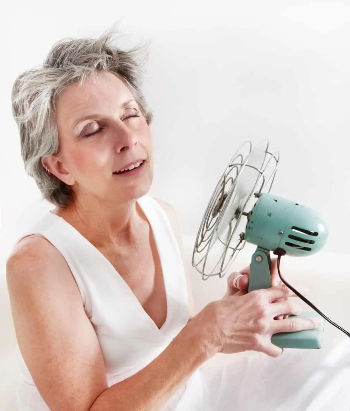 Menopausal woman using fan to cool down during a hot flash