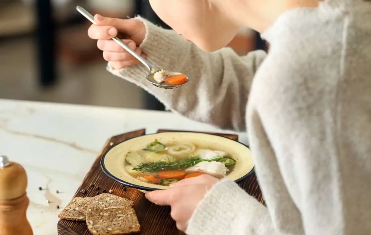 Close up of woman eating bowl of homemade fish soup with vegetables in broth 