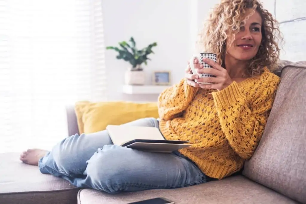 40 something woman relaxed on couch with book and cup of tea