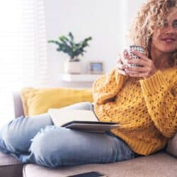 40 something woman relaxed on couch with book and cup of tea