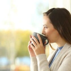 Brunette woman calmly sipping hot tea while gazing out at nature